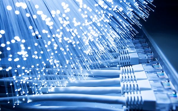 Close-up of glowing fiber optic cables next to several plugged-in Ethernet cables and network ports, representing high-speed internet and data connectivity.