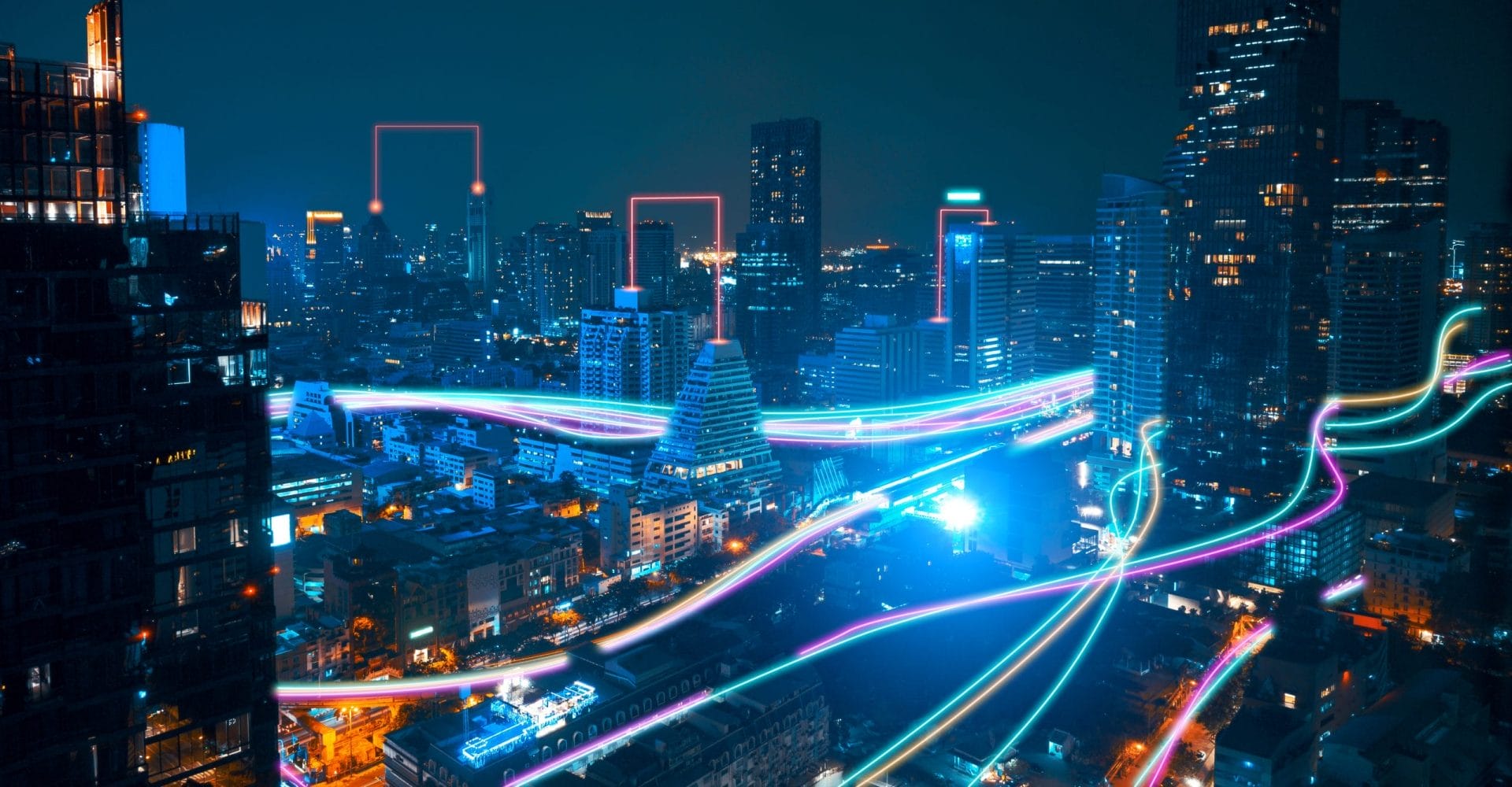 A futuristic cityscape at night with tall buildings and colorful neon light trails winding through the streets, symbolizing advanced technology and digital connectivity.