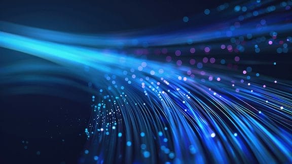 Glowing blue and purple fiber optic strands curve across a dark background, with small points of light scattered throughout, creating a dynamic, futuristic effect.