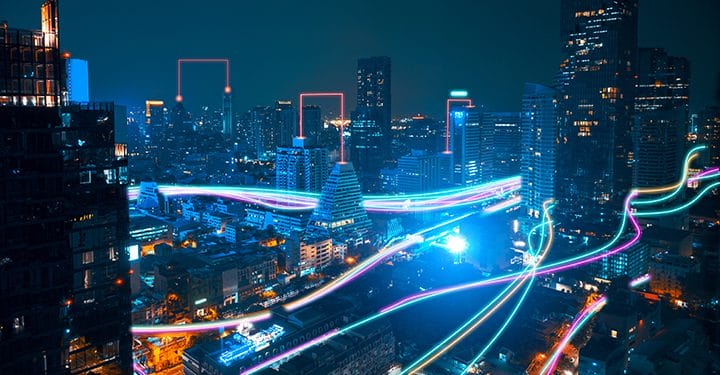 A vibrant cityscape at night with illuminated skyscrapers and colorful light trails weaving through the streets, representing fast digital or data connections in an urban environment.