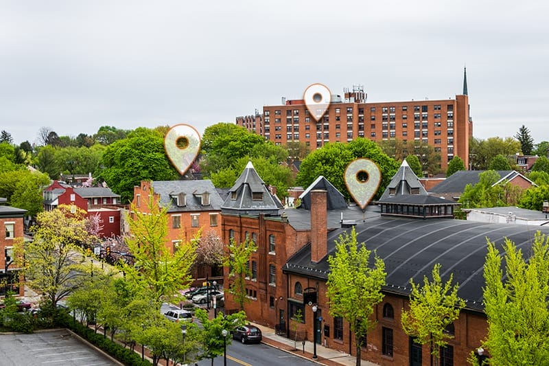 A small town with brick buildings and green trees. Three digital location markers above various buildings suggest mapped locations or enterprise fiber access points in Lancaster, PA.
